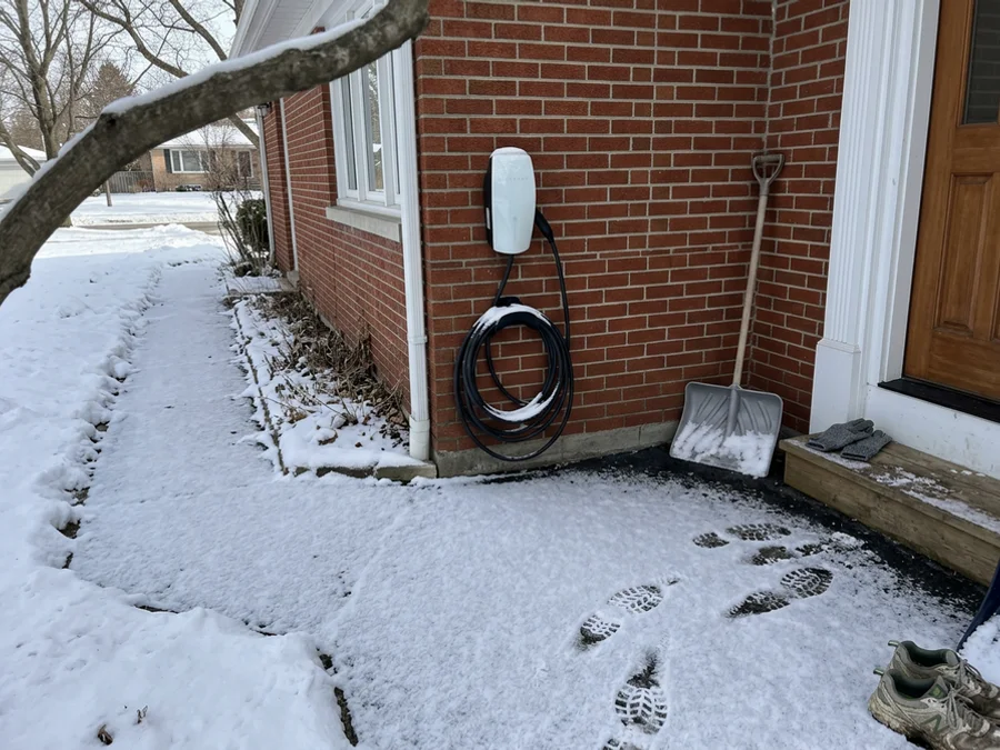 Outdoor-rated Tesla Wall Connector mounted on exterior brick in winter