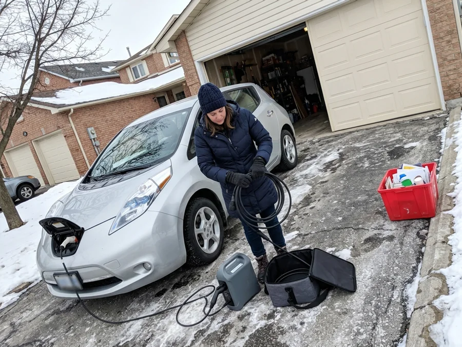 Homeowner coiling a portable EV charger beside a parked electric car